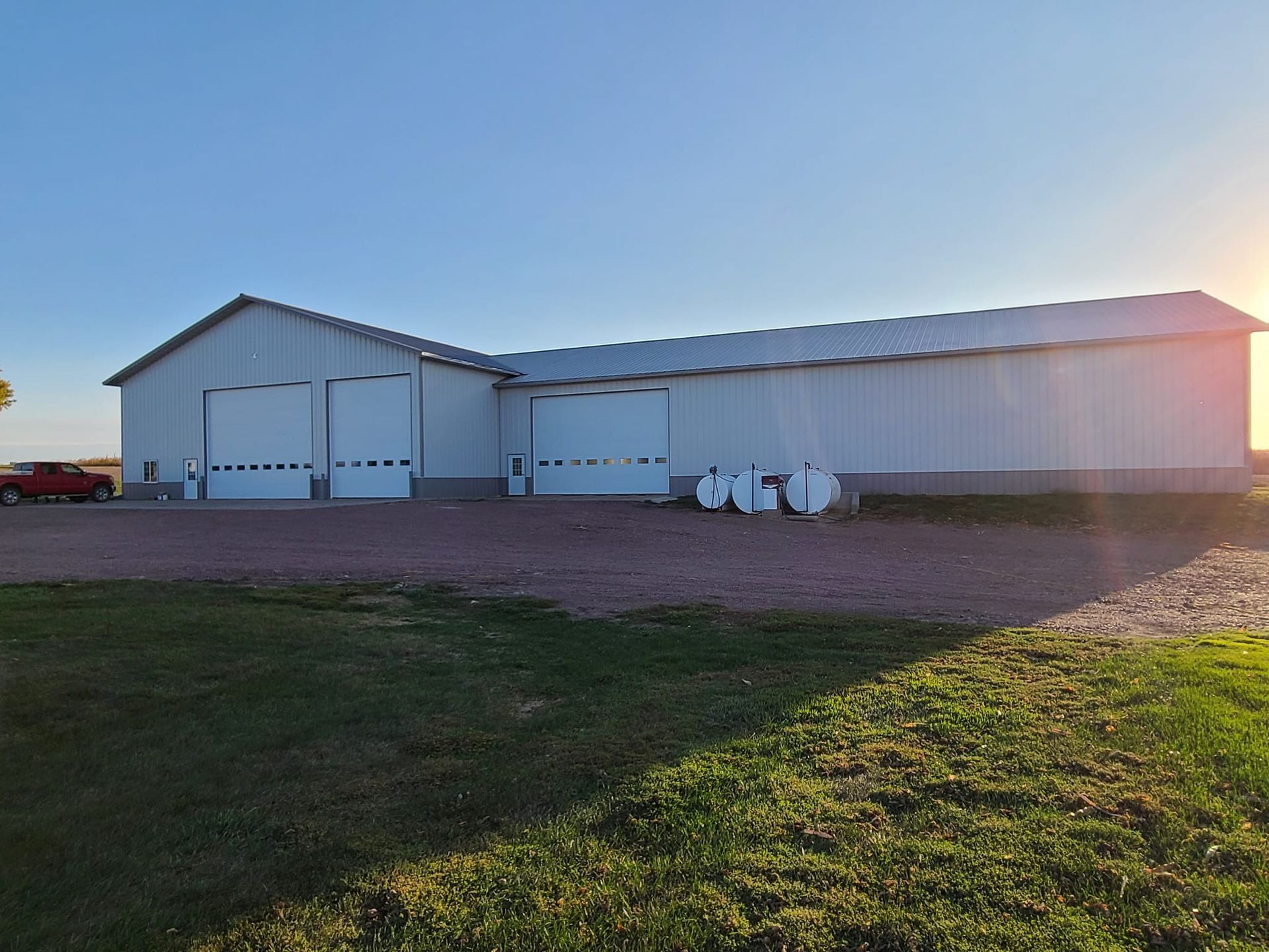 A large white barn with a red car parked in front of it.