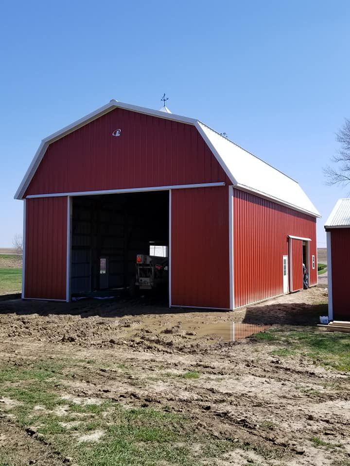 A red barn with a white roof sits in the middle of a dirt field
