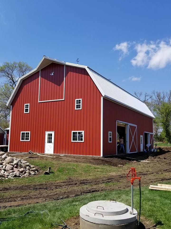 A large red barn with a white roof is being built on a farm.