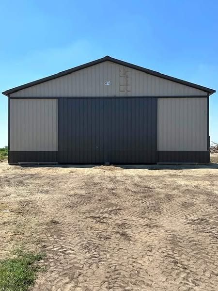 A large building with a sliding door is sitting in the middle of a dirt field.