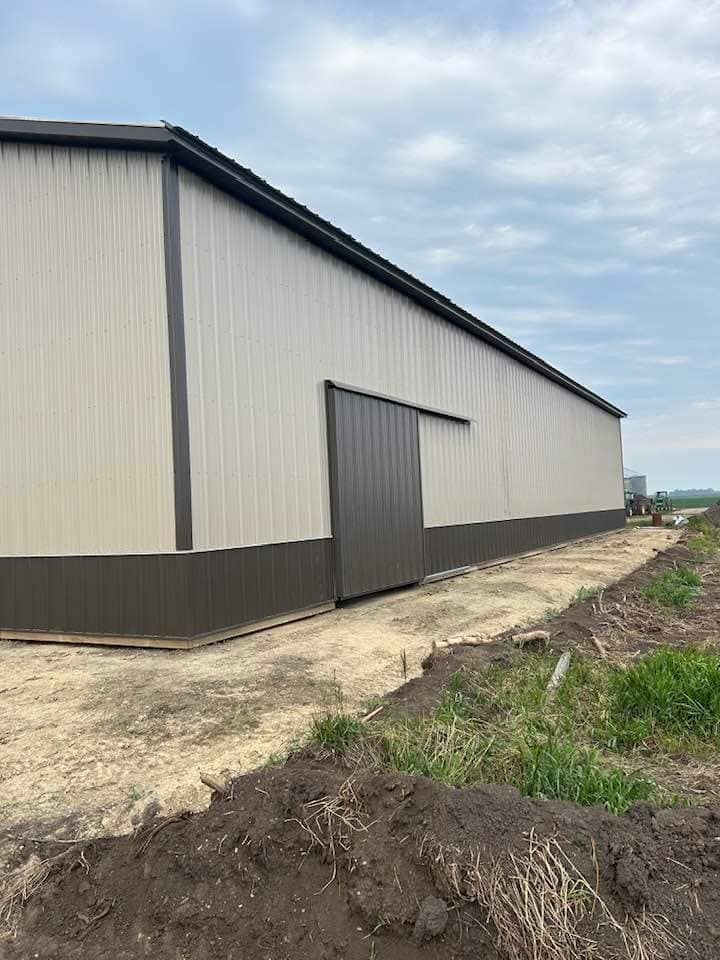 A large metal building with a sliding door is sitting in the middle of a dirt field.