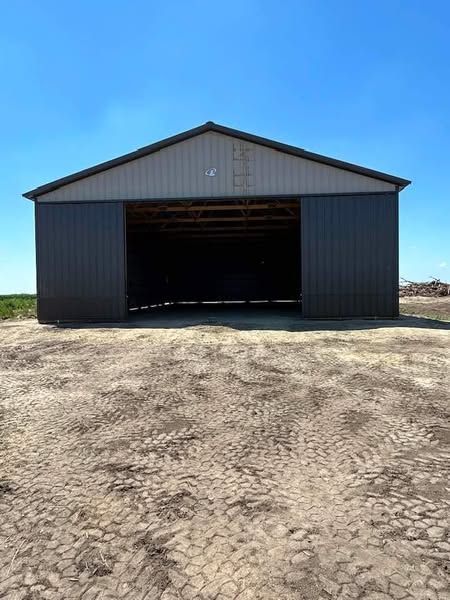 A large barn with a sliding door is sitting in the middle of a dirt field.