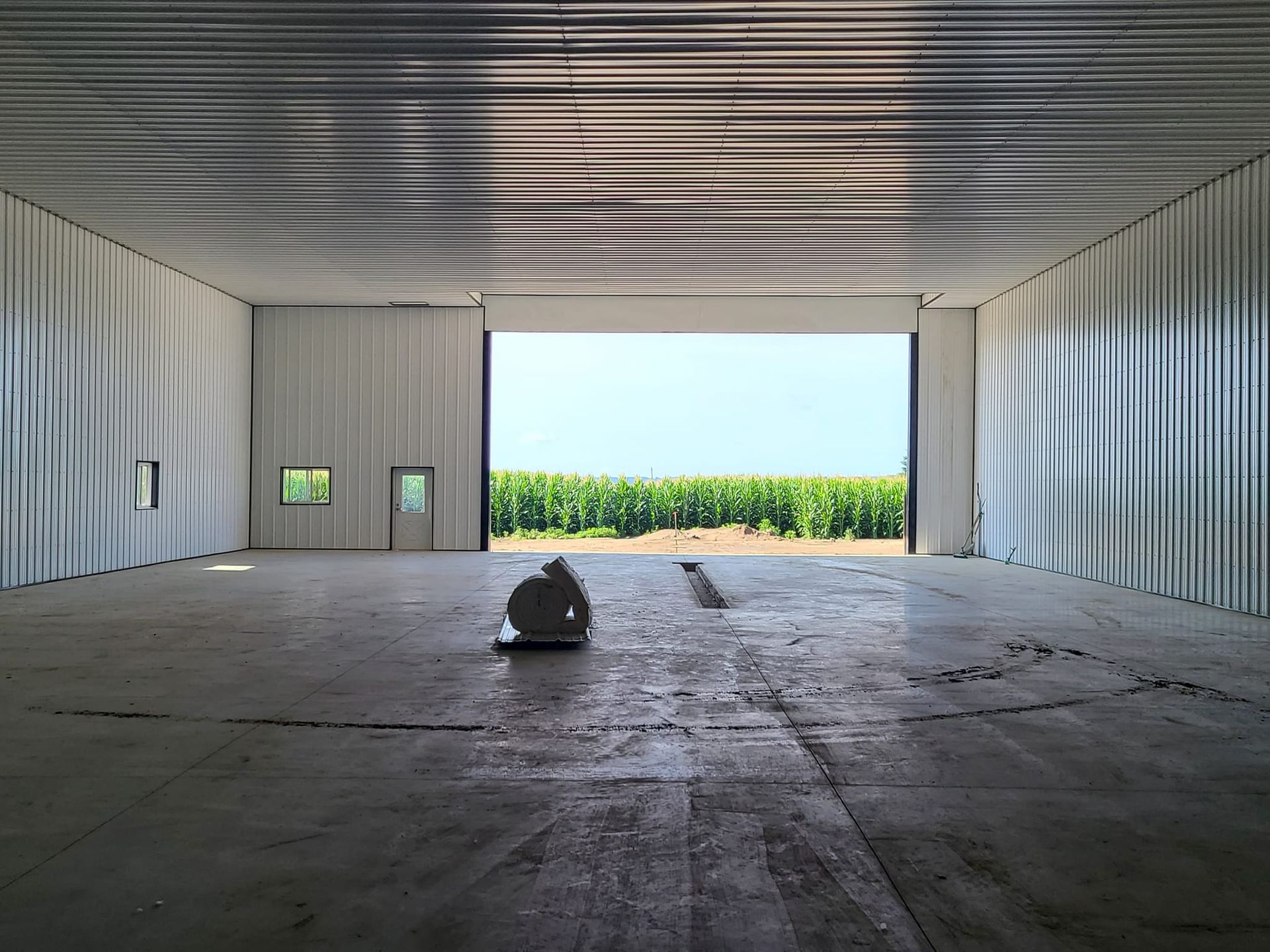 An empty warehouse with a large door open to a field of corn.