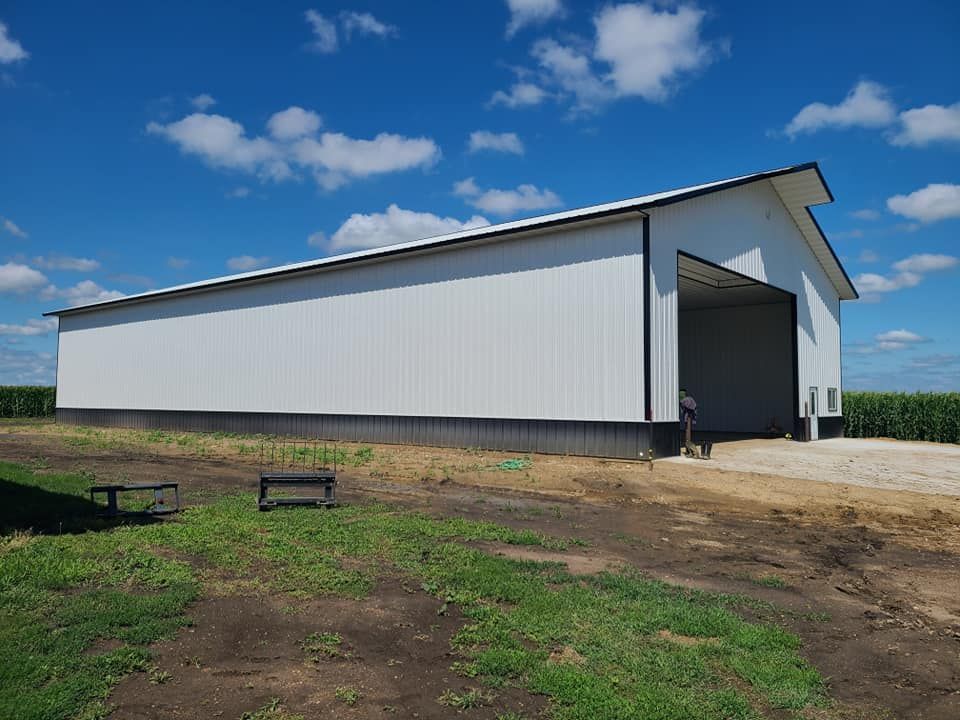 A large white barn is sitting in the middle of a grassy field.