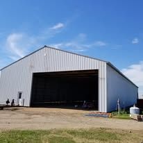 A large white building with a large door is sitting in the middle of a field.