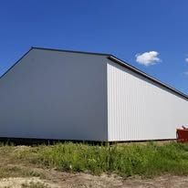 A large white barn is sitting in the middle of a grassy field.
