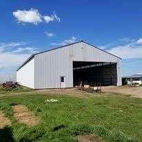 A large white barn is sitting in the middle of a grassy field.