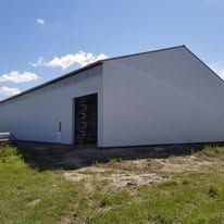 A large white barn is sitting in the middle of a grassy field.