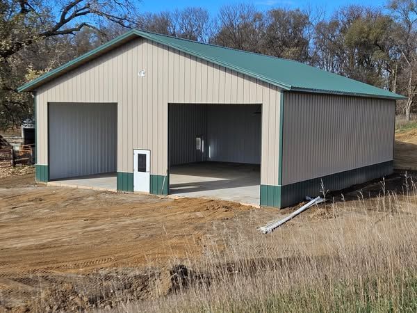 A large metal garage with a green roof is sitting in the middle of a field.