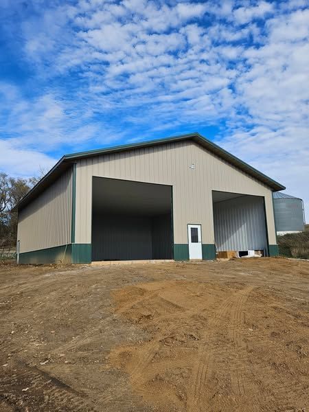 A large building with two garage doors is sitting in the middle of a dirt field.