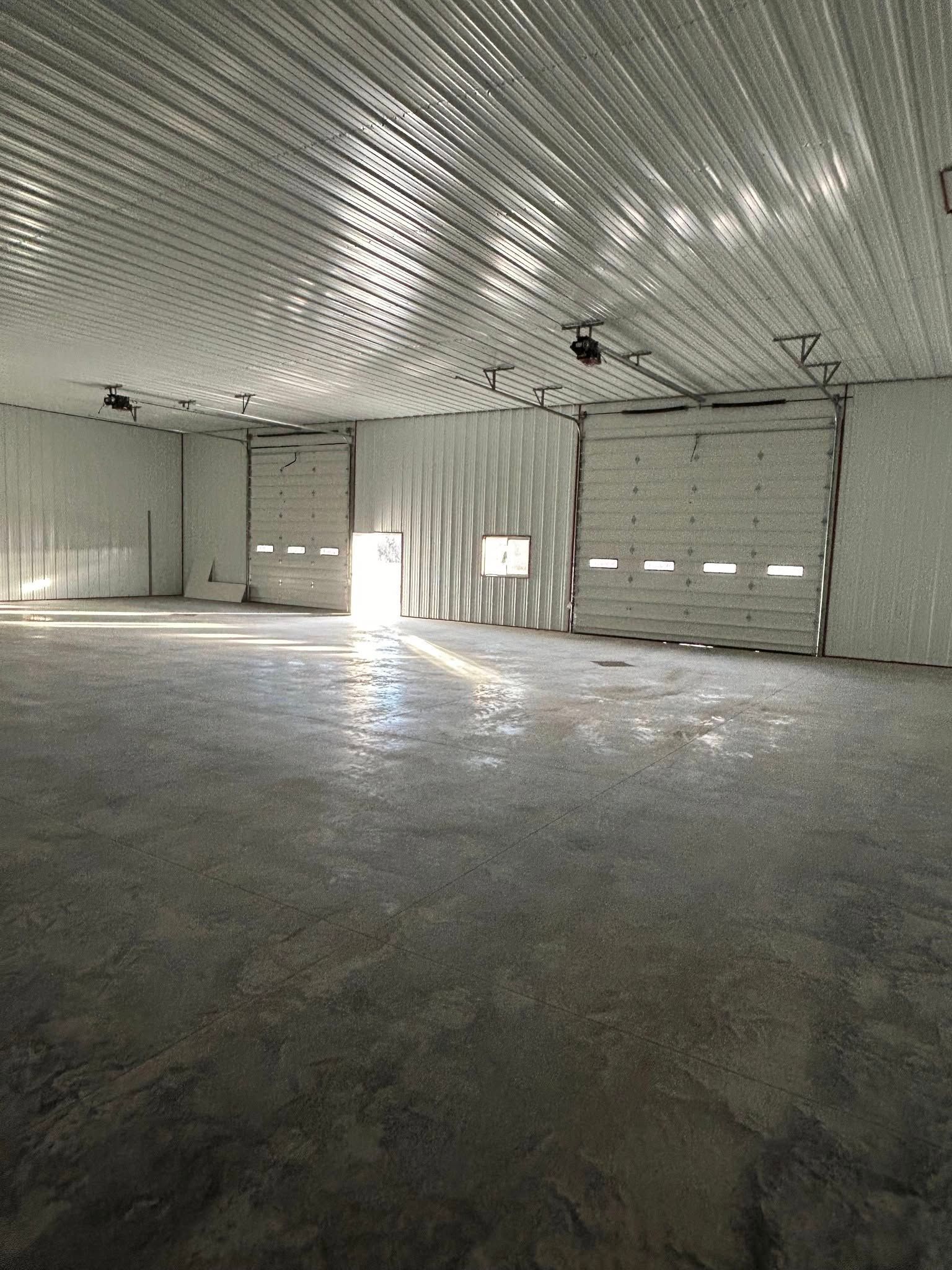 A large empty warehouse with a garage door and a ceiling fan.