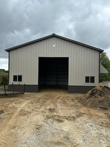 A large metal building with a large door is sitting on top of a dirt field.