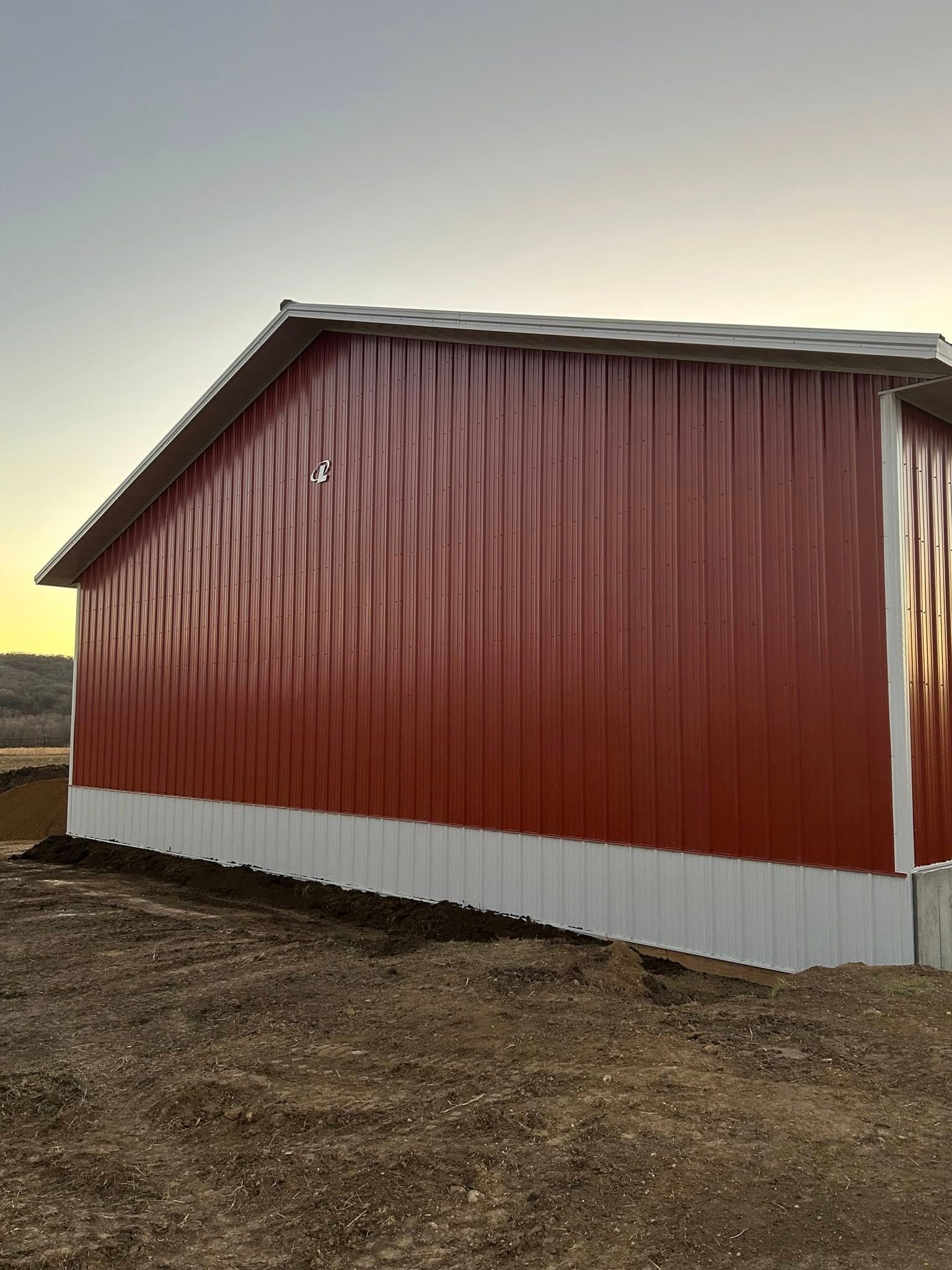 A red and white barn is sitting in the middle of a dirt field.