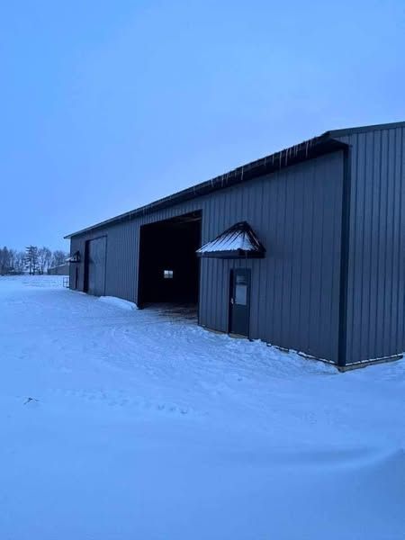 A large metal building is sitting in the middle of a snow covered field.