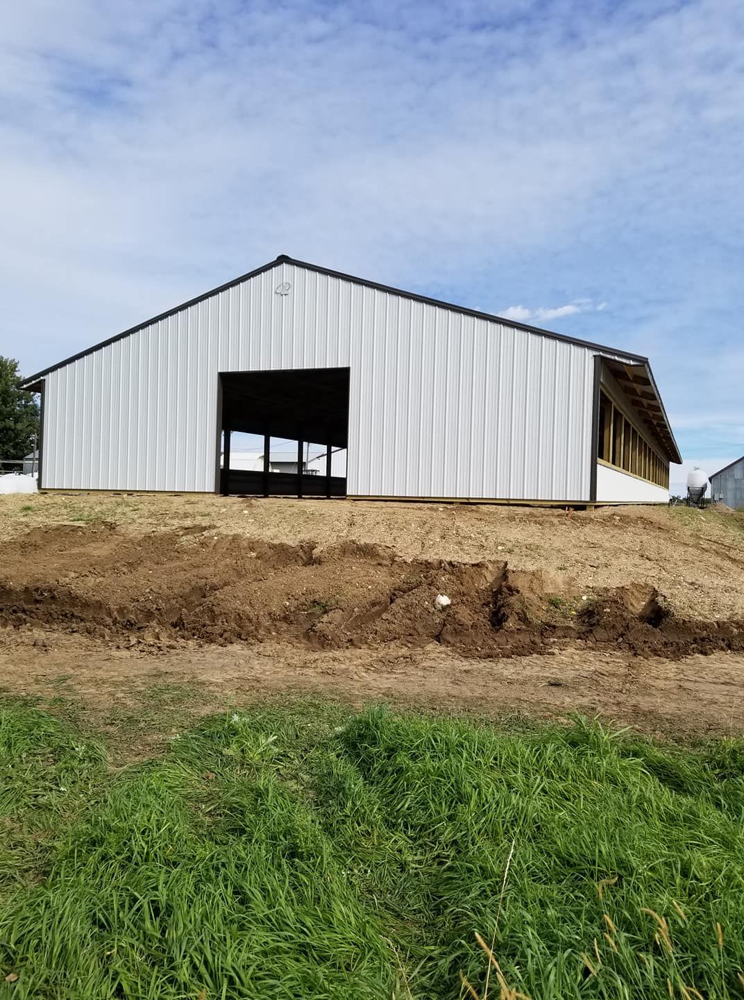 A large white barn is sitting on top of a dirt hill.