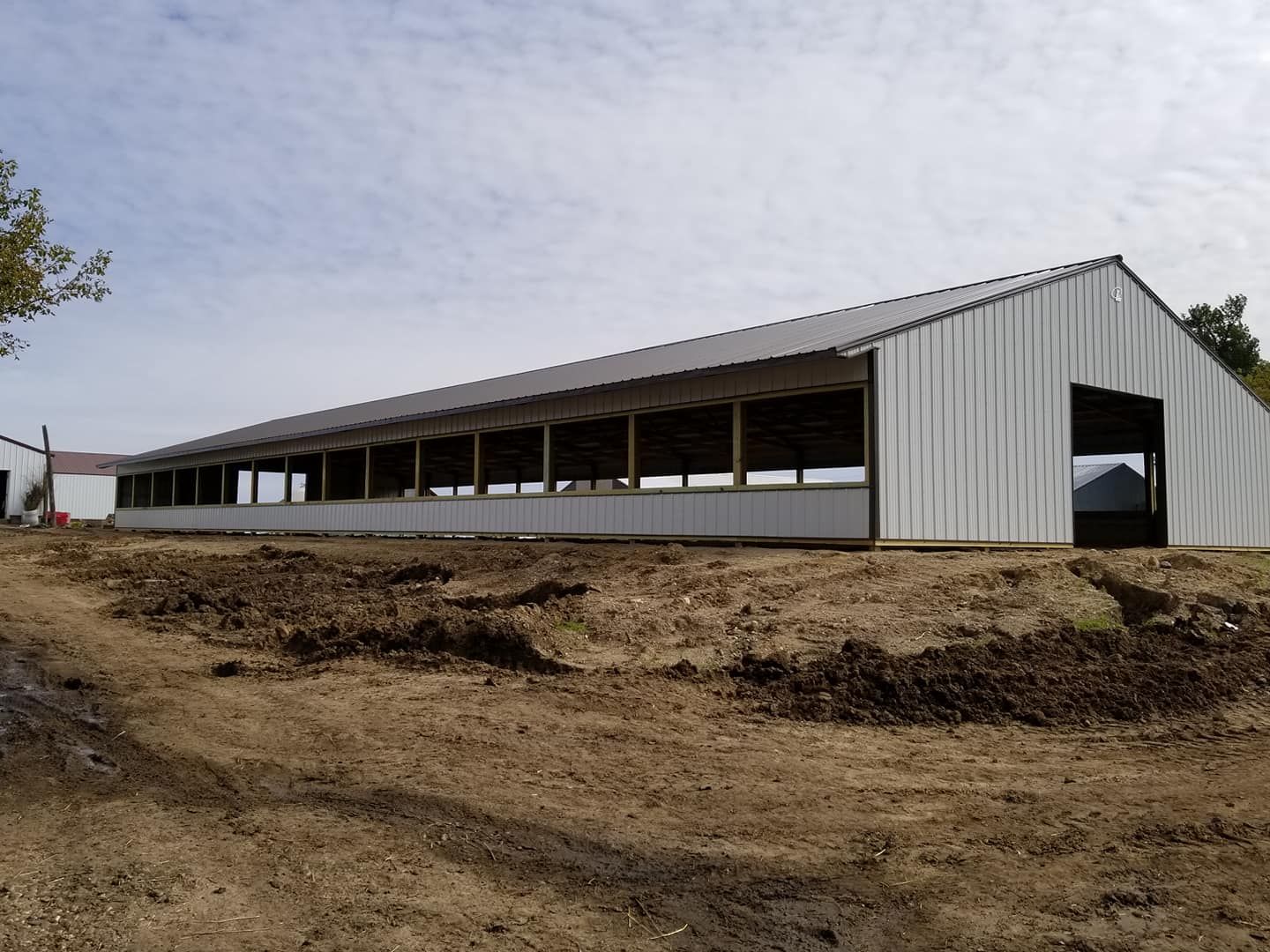 A large white barn is sitting in the middle of a dirt field.
