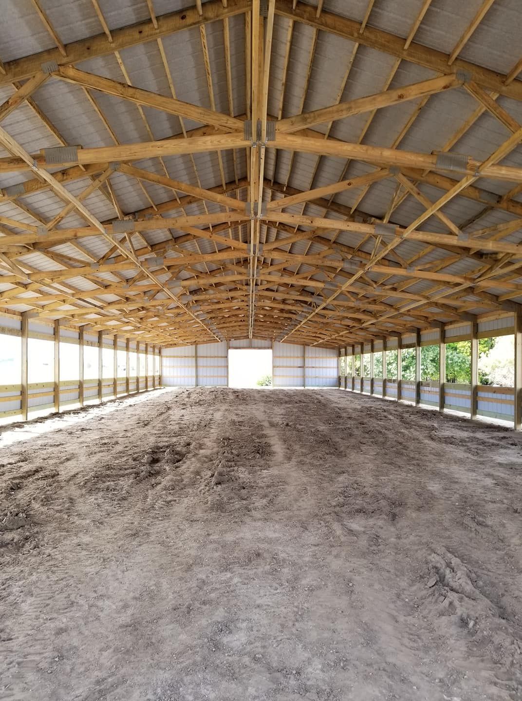 A large empty barn with wooden beams and a dirt floor.