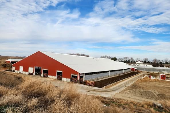 A large red barn with a white roof is sitting in the middle of a field.