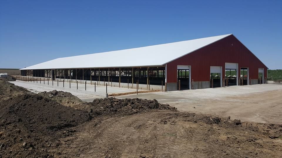 A large red barn with a white roof is sitting in the middle of a dirt field.