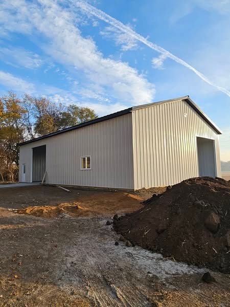 A large white barn is being built in a dirt field next to a pile of dirt.