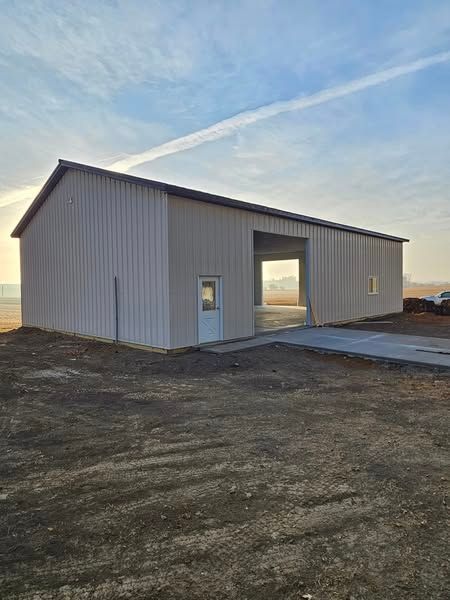 A large metal building with a garage door is sitting in the middle of a dirt field.