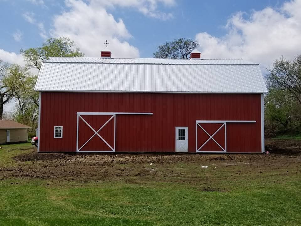 A red barn with a white roof sits in a grassy field