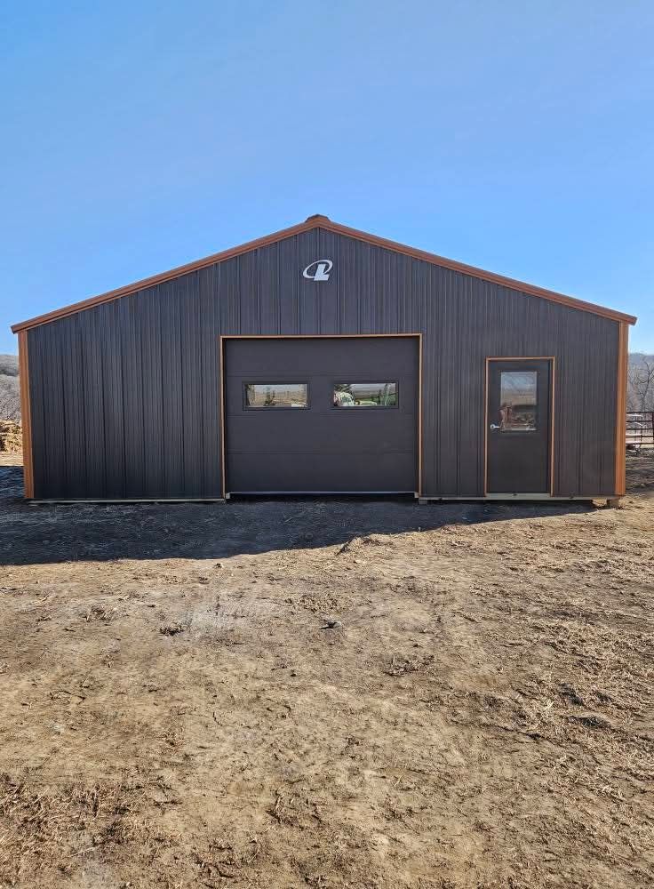 A large metal building with a large garage door is sitting in the middle of a dirt field.