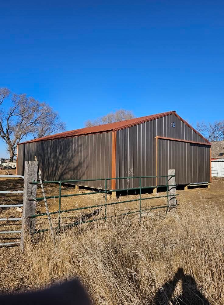 A large metal barn is sitting in the middle of a field next to a fence.