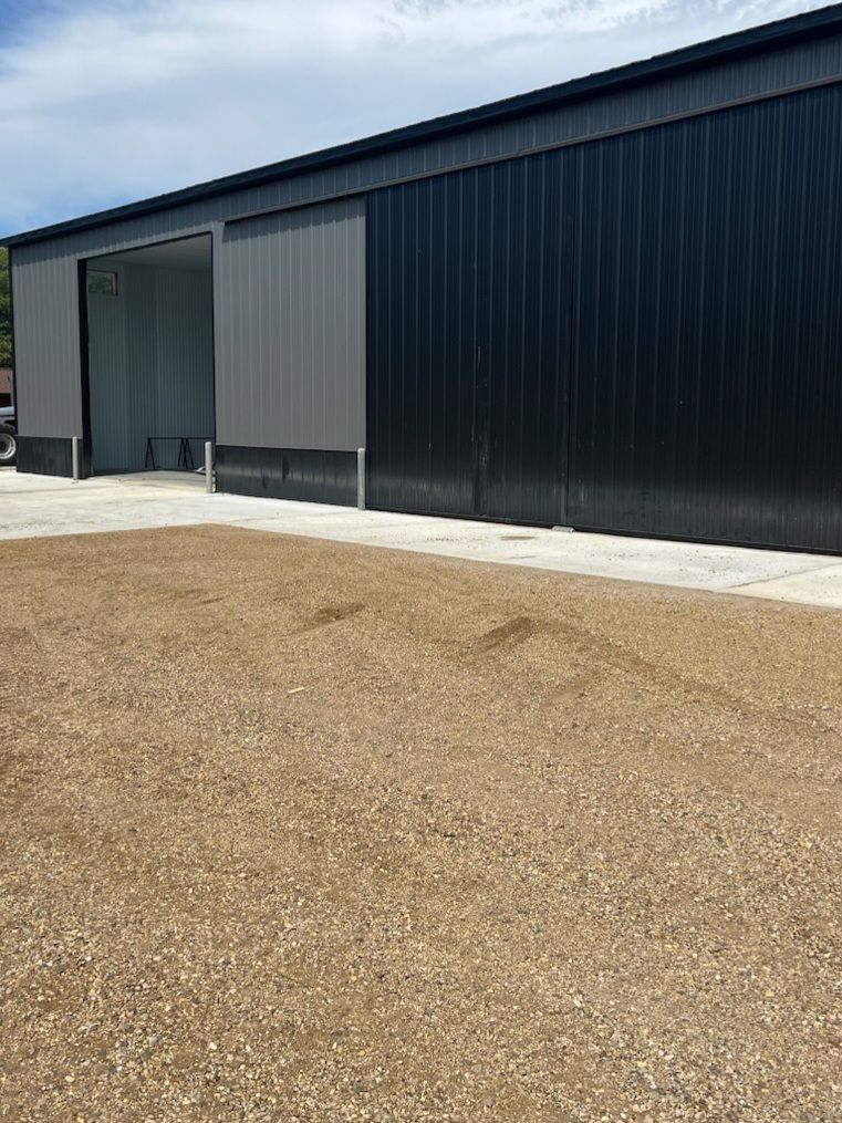 A large building with sliding doors is sitting on top of a dirt field.