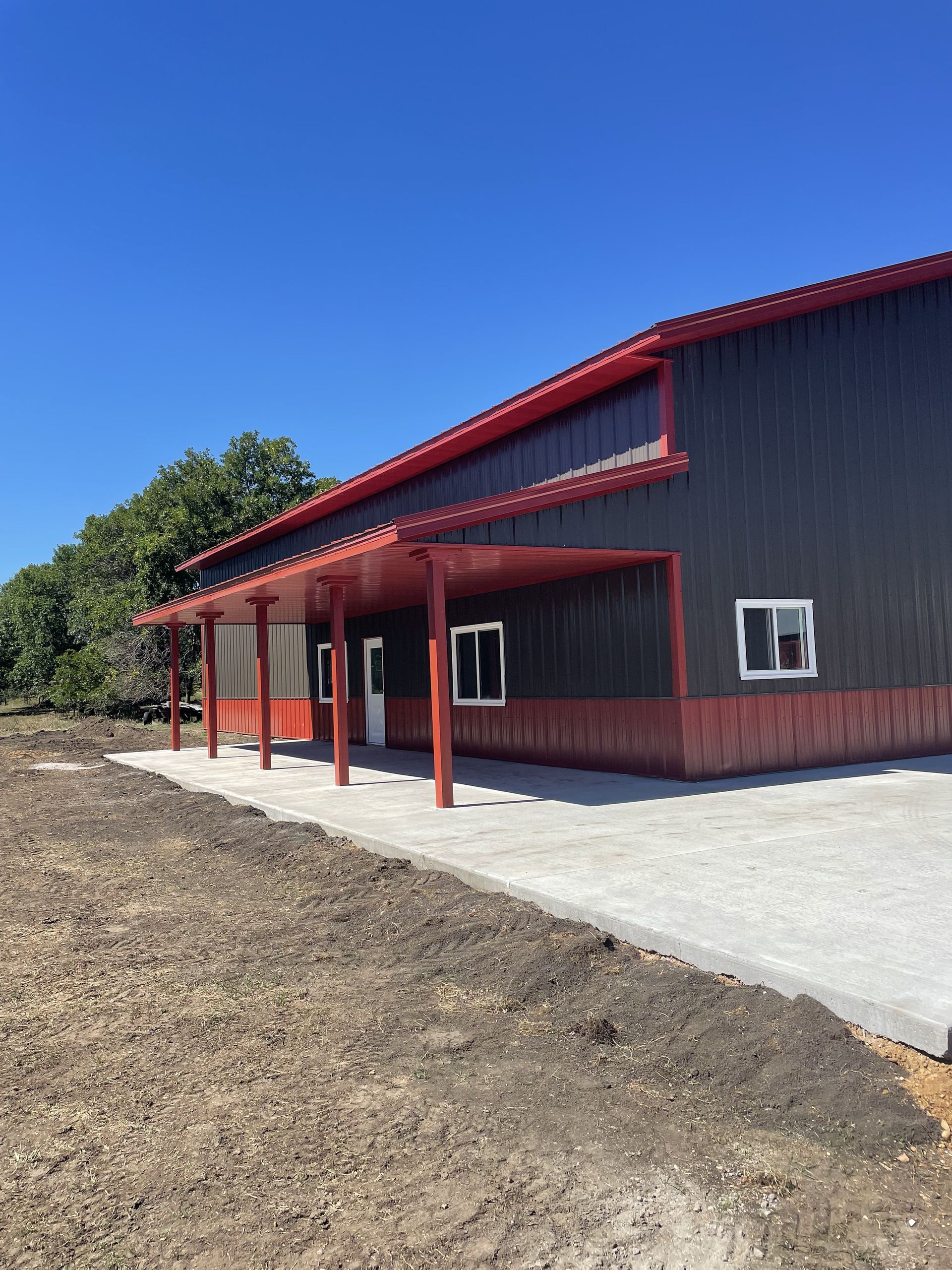 A large building with a red roof is sitting in the middle of a dirt field.
