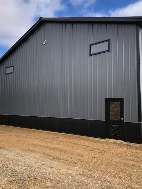A large gray building with a black door is sitting on top of a dirt road.