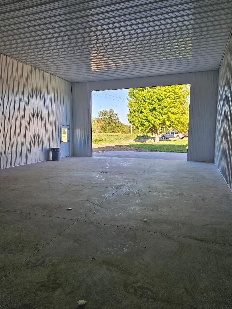 An empty garage with a large door open to a field.