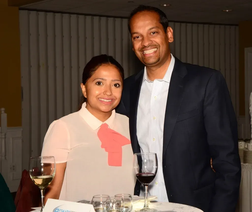 Woman and man smiling, standing near a table with wine glasses.