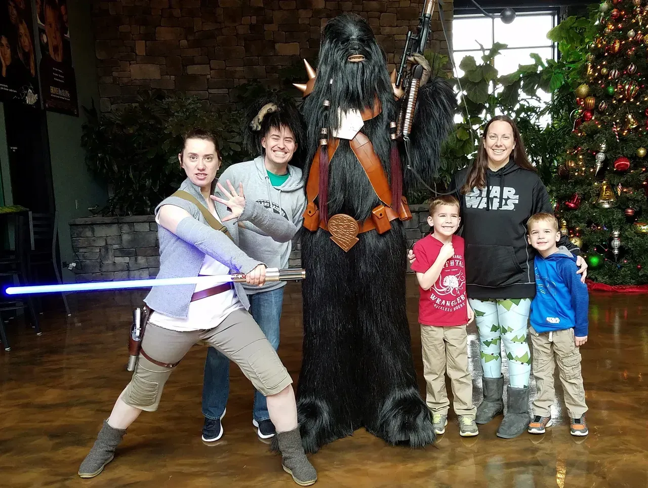 Group poses with Chewbacca and a person with a lightsaber in front of a Christmas tree.