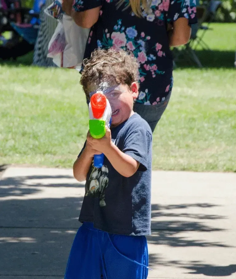 Child aiming a water gun, spray on face, outdoors.