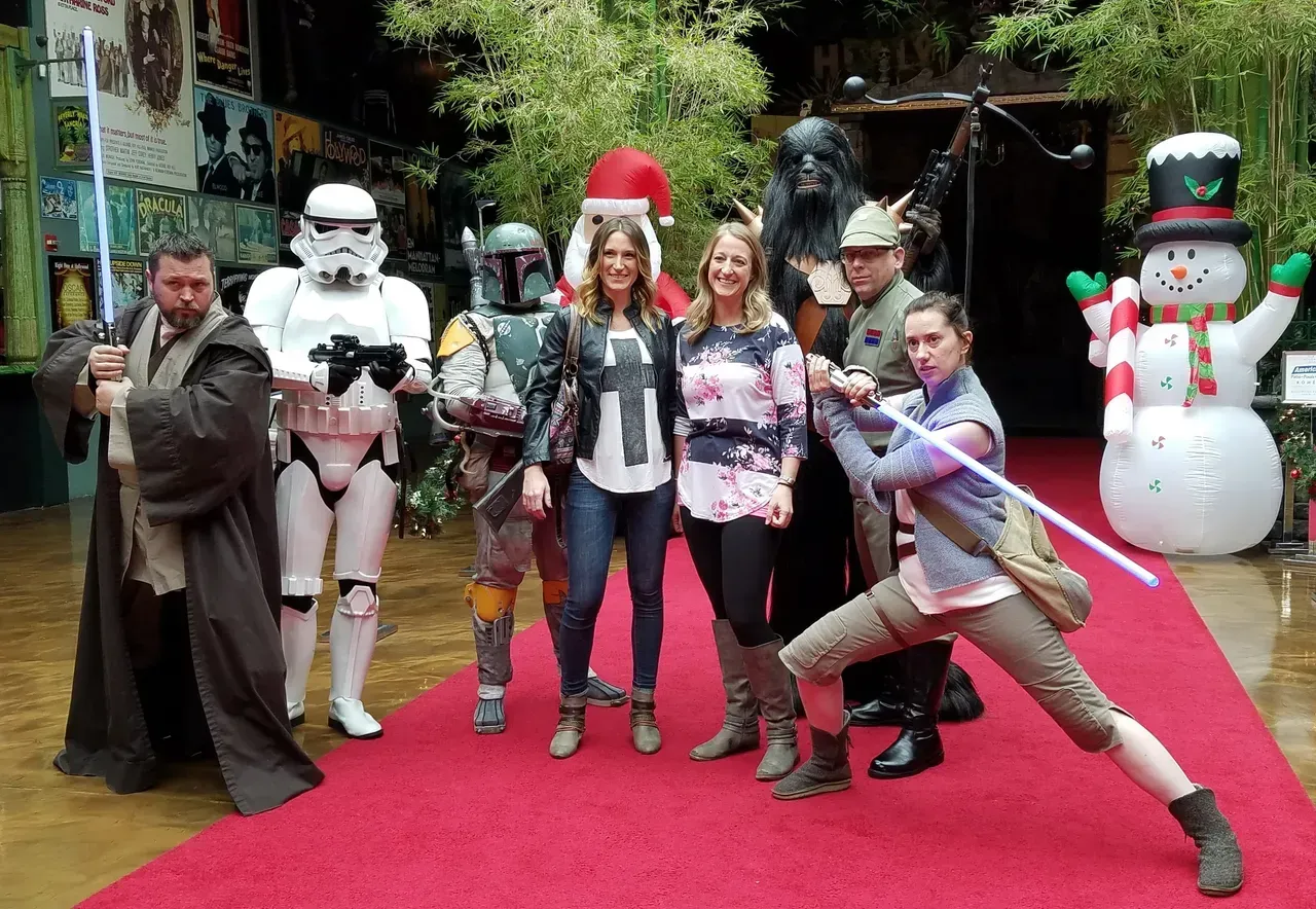 People pose with Star Wars characters on a red carpet. A snowman decorates the background.