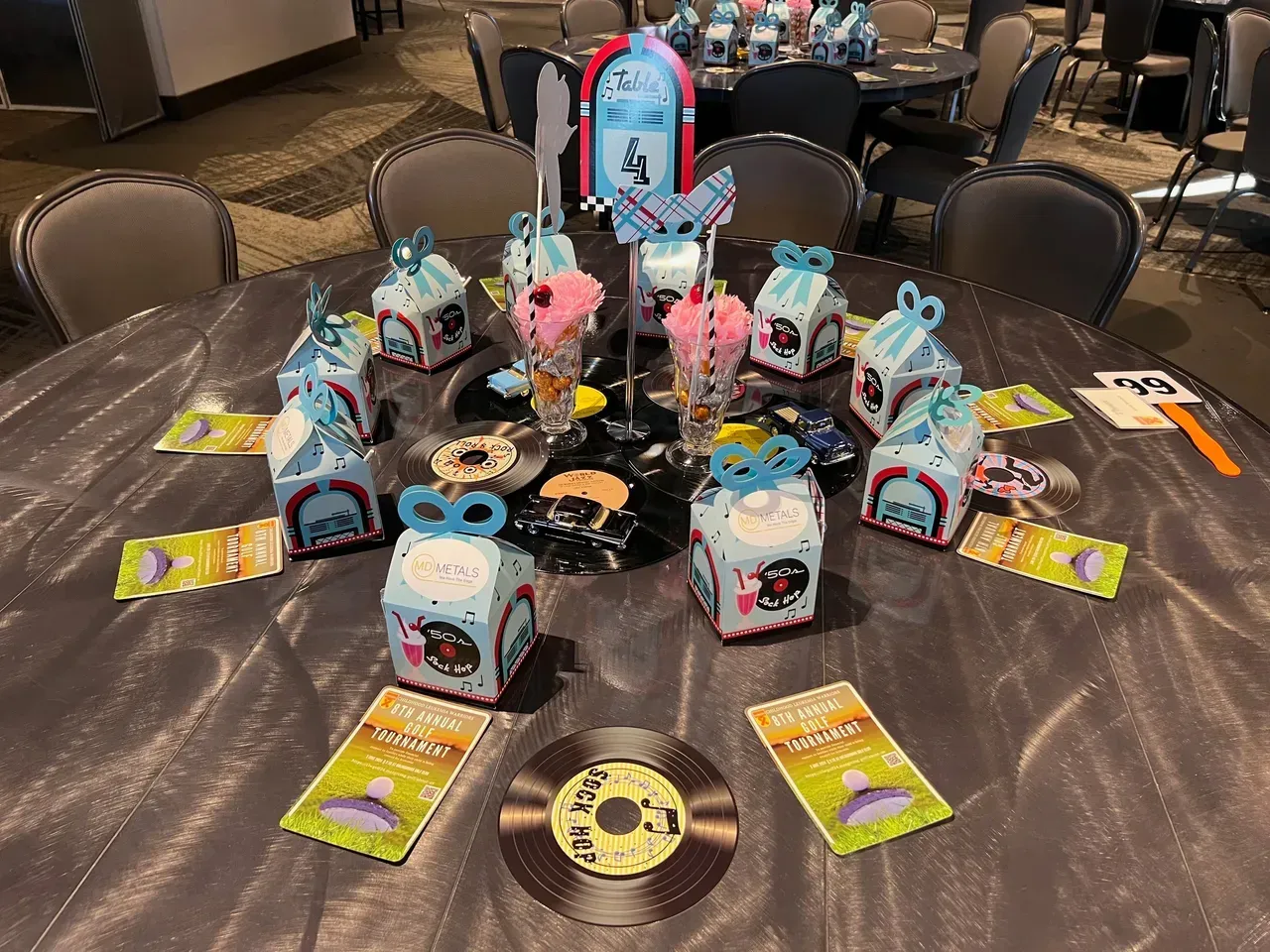 Round table with themed decorations: blue gift boxes, records, and colorful treats for a party.