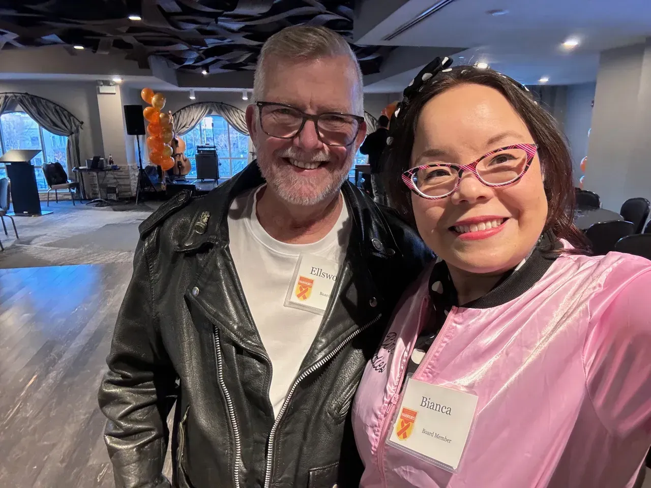 Two people in retro outfits smile, posing for a selfie at an event.