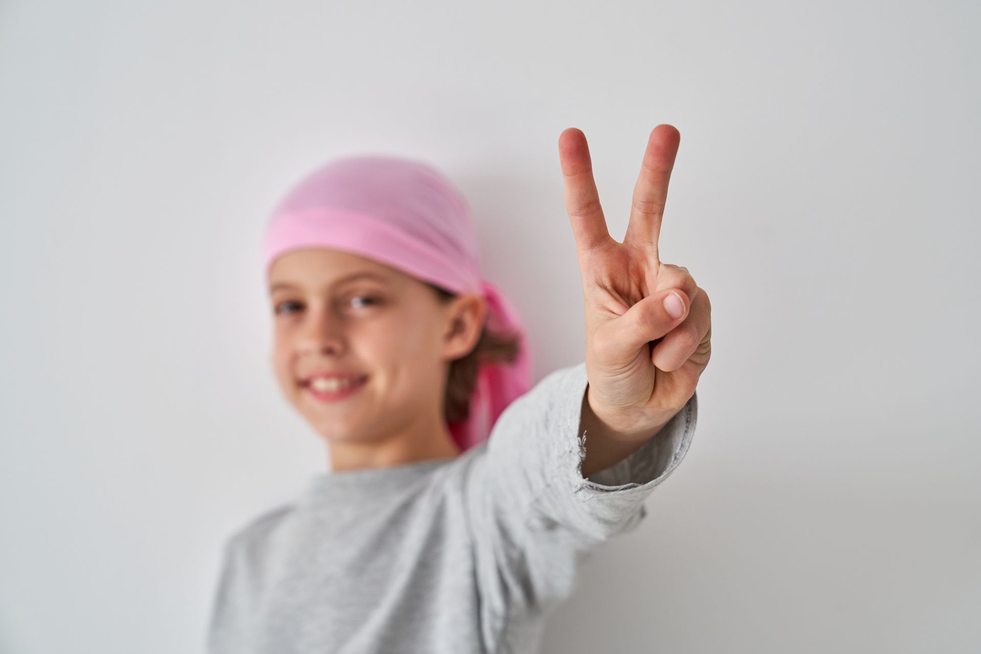 Girl with pink headscarf makes peace sign, smiling.