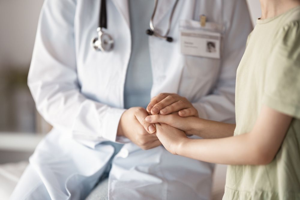 Doctor in white coat holds a patient's hands, offering comfort.