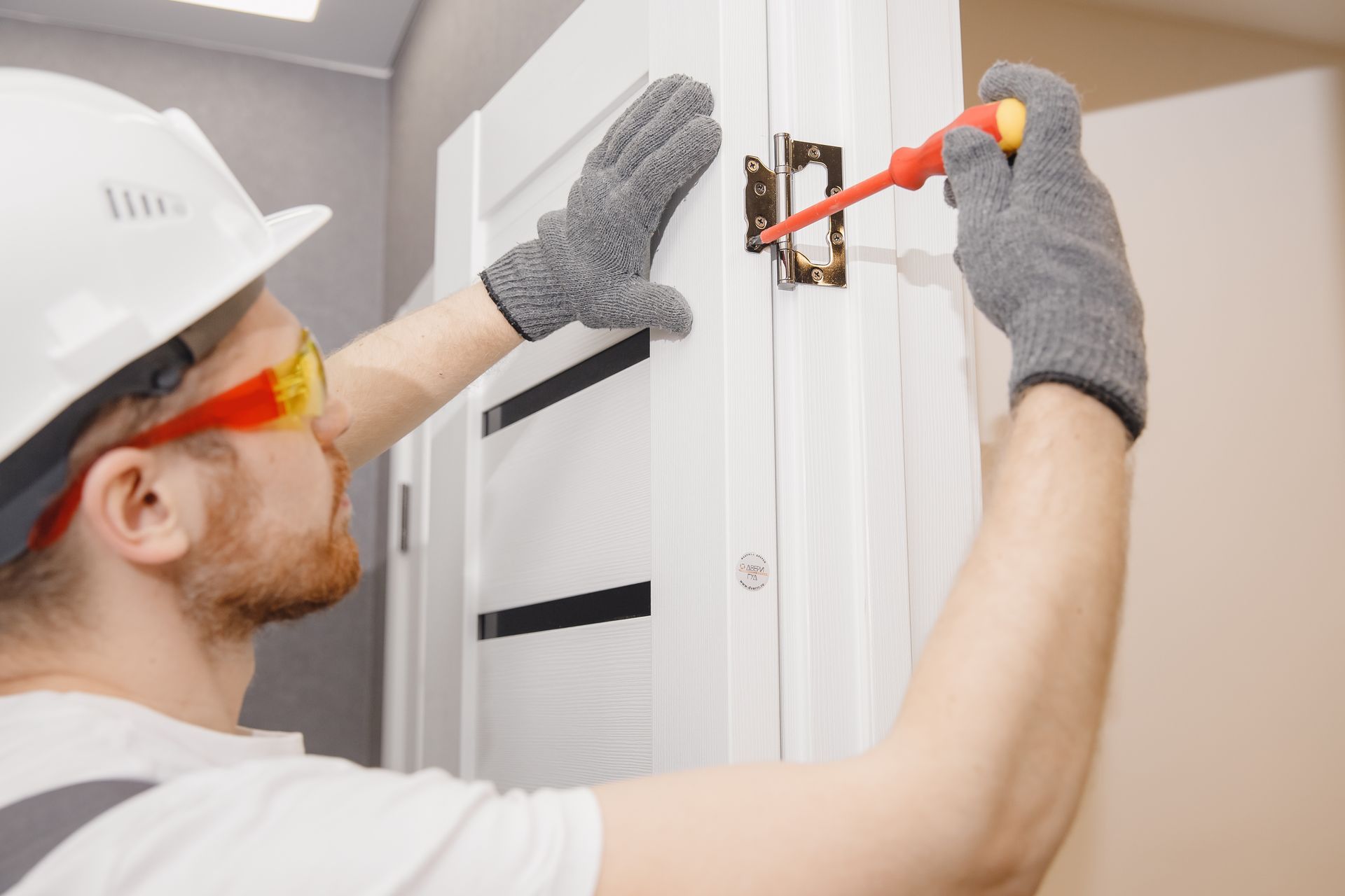 A handyman is installing a wood door and is seen in the process of tightening the lock.