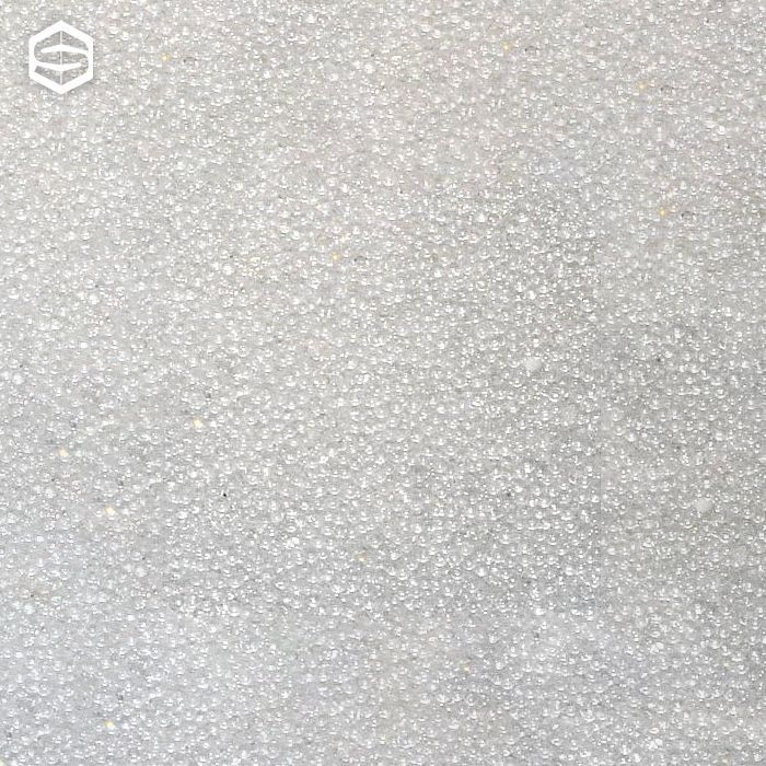 Primo piano di una superficie ricoperta da numerose piccole particelle granulari bianche, che appaiono leggermente ruvide.