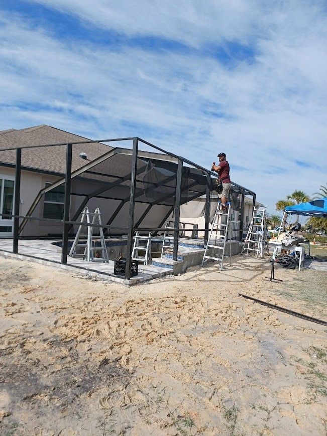 A man is standing on a ladder on top of a screened in porch.