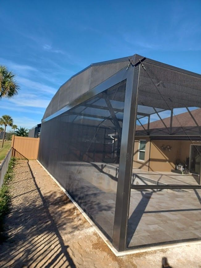A screened in porch with a canopy and a fence in front of a house.
