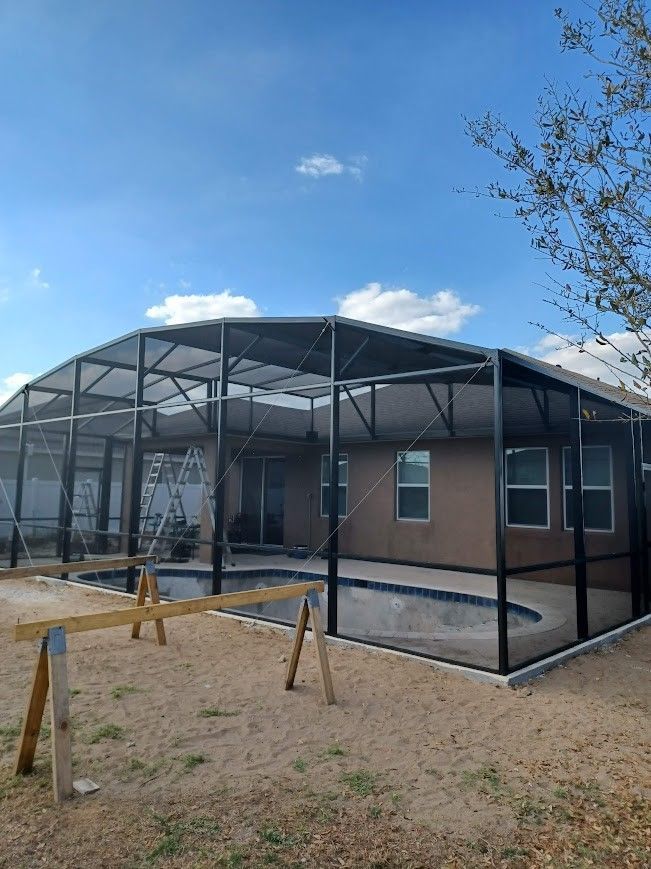 A house with a screened in swimming pool in front of it.