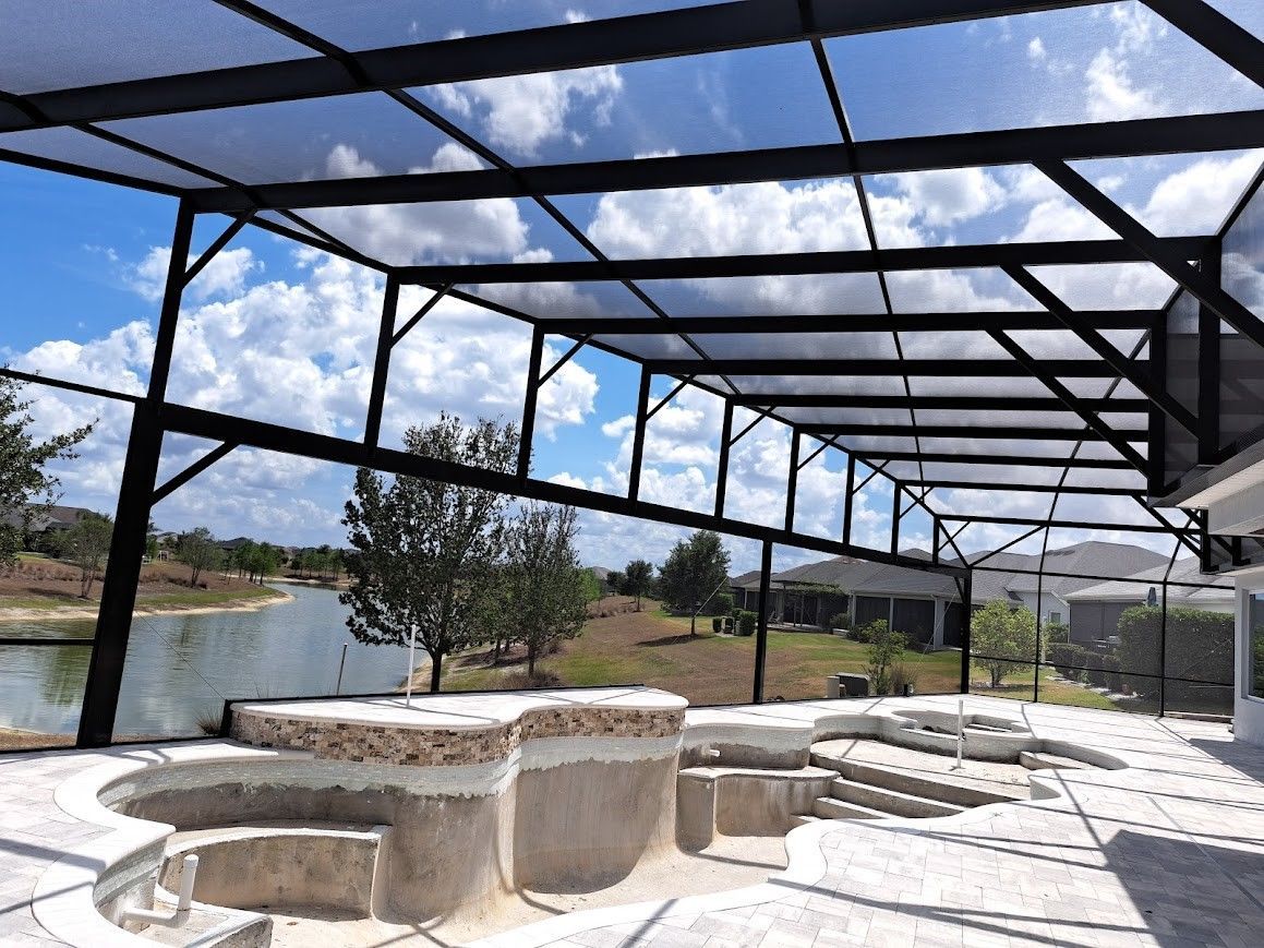 There is a swimming pool under a covered area with a view of the water.