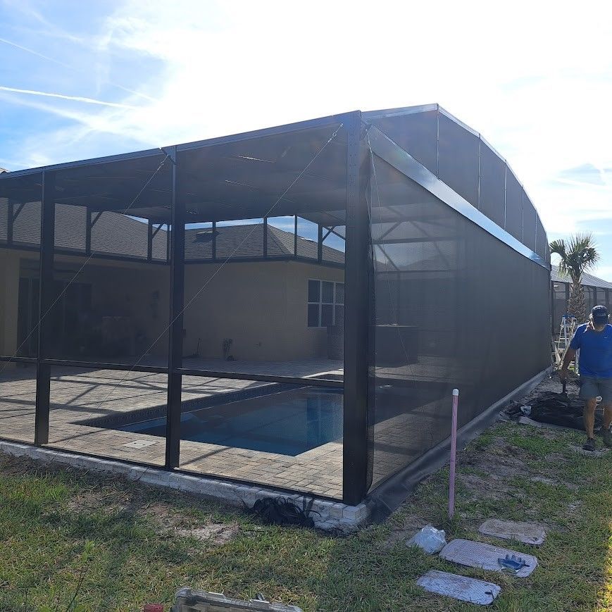 A man is standing in front of a screened in swimming pool.
