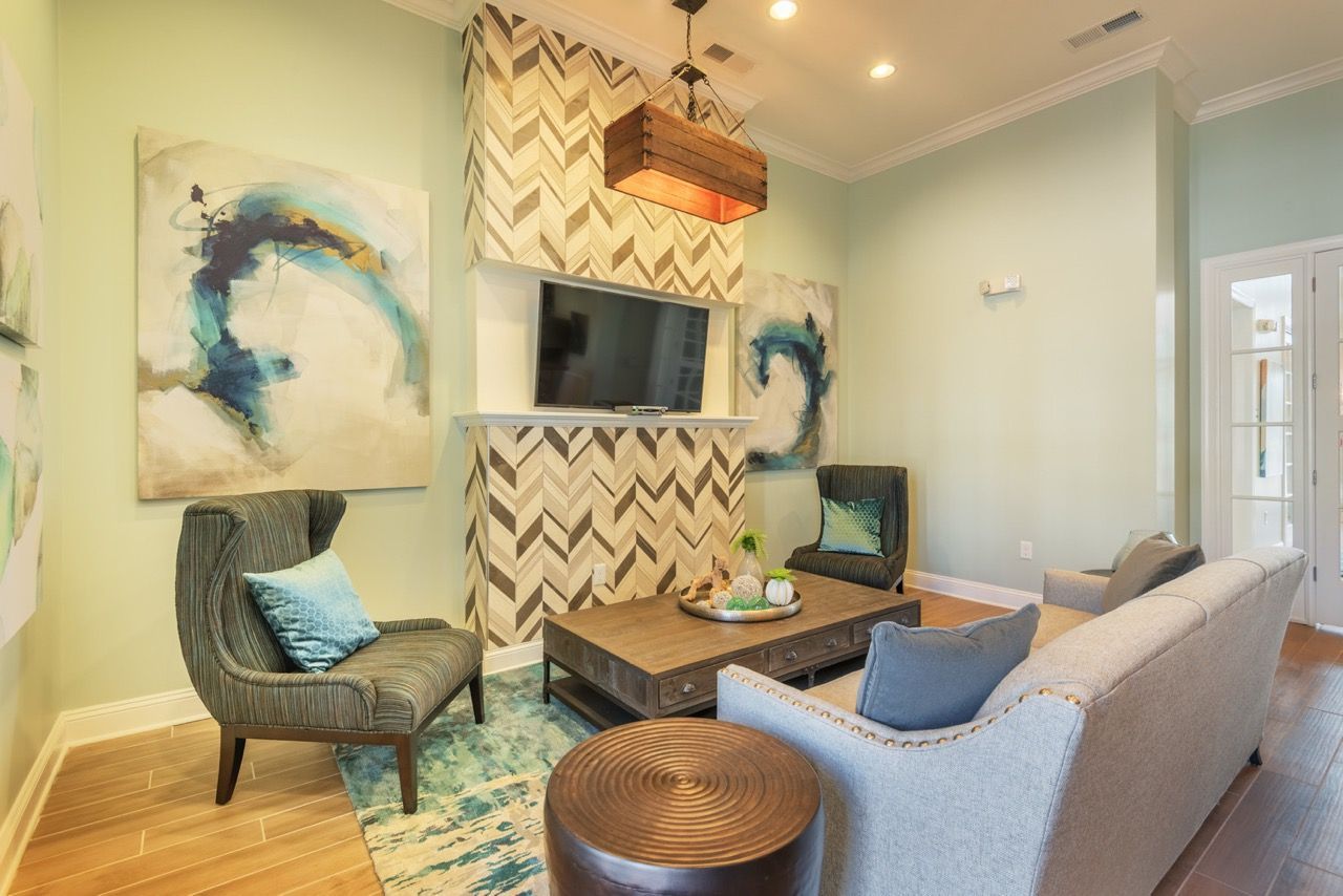 Living room in a modern apartment with mint green walls, gray sofa, teal chairs, and a wall-mounted TV.
