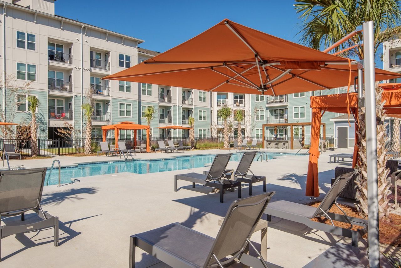 Outdoor pool area with lounge chairs and orange shade umbrellas at a modern apartment community.