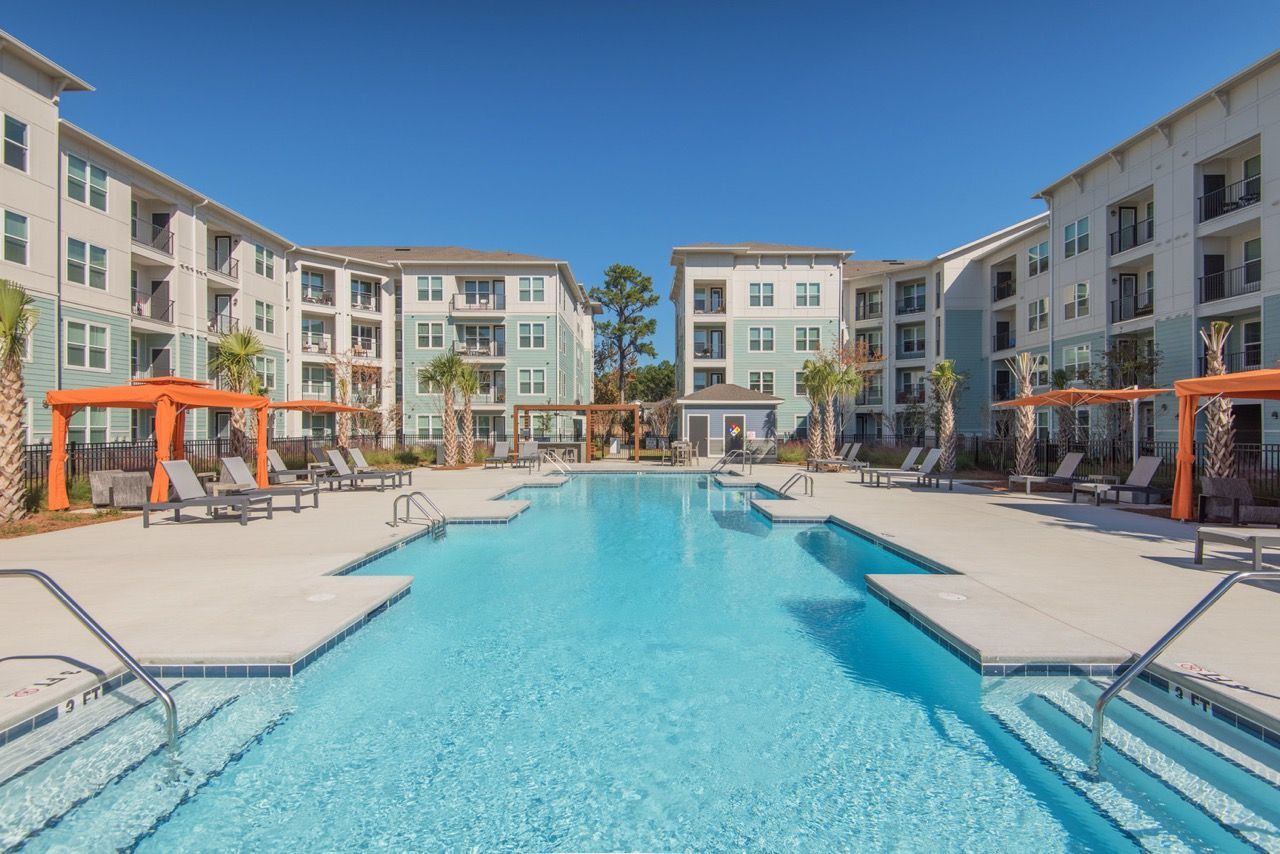 Outdoor community swimming pool bordered by apartment buildings, lounge chairs, and orange cabanas.